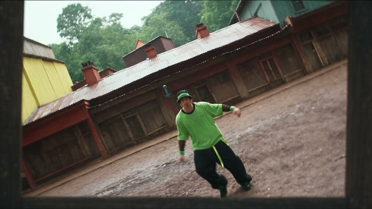 A dancer in a green shirt framed inside a wooden picture frame in a rain-soaked village